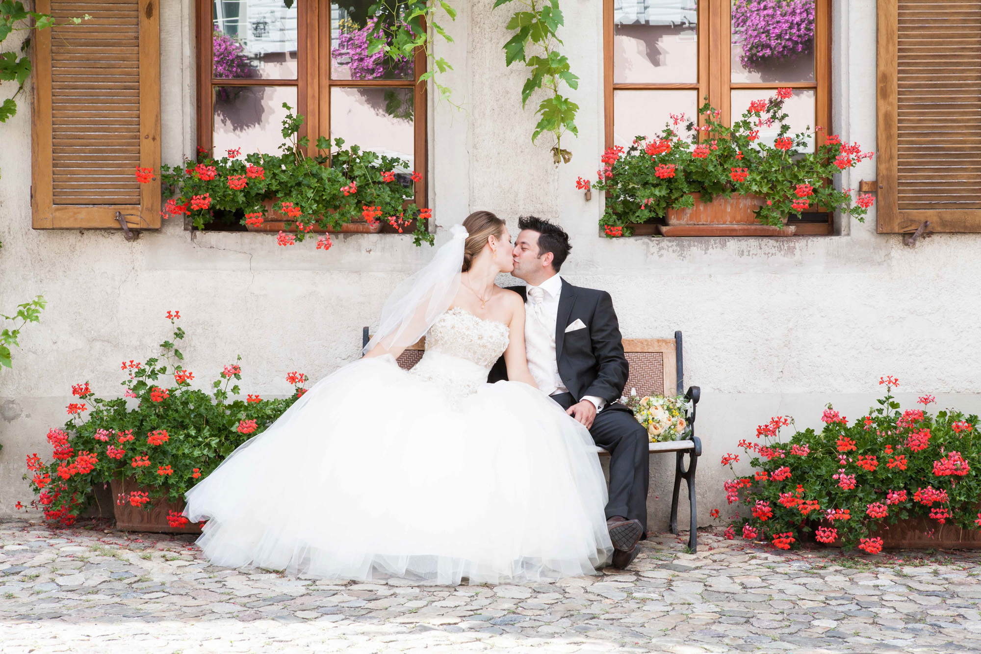 Hochzeitsfotografie - Brautpaar küsst sich auf der Bank